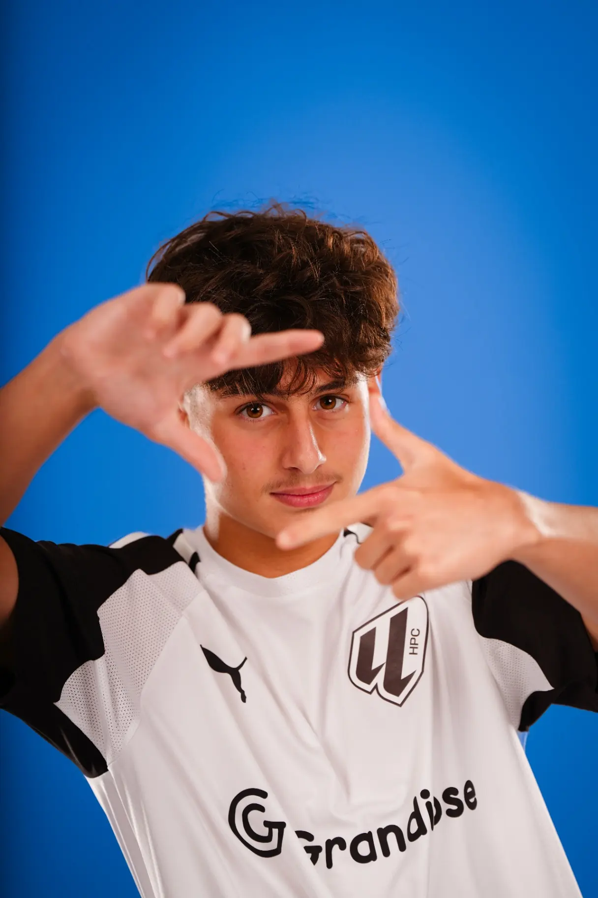 Studio portrait — young footballer framing shot on blue